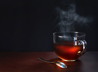 a cup of freshly brewed black tea, escaping steam on a dark background and copy space for text