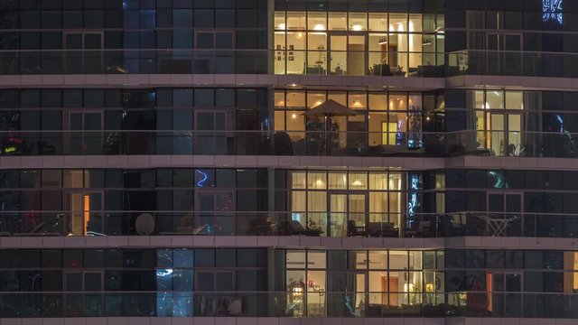Rows of glowing windows with people in the interior of apartment building at night. Modern skyscraper with glass surface. Concept for business and modern life