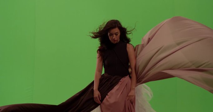 Beautiful woman looks up intently as her dress blows in the wind surrounding her against green screen
