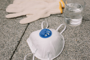 Mask, gloves are lying on the grey table background. Glass of water is standing on the grey background. Safety.