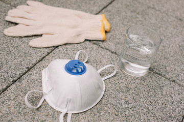 Mask, gloves are lying on the grey table background. Glass of water is standing on the grey background. Safety.
