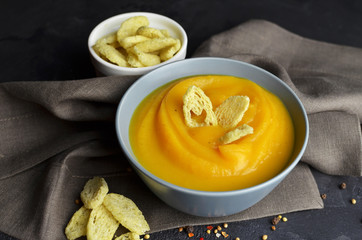 Butternut squash soup with wheat croutons, fresh garlic and spices in ceramic bowl on grunge black background with linen napkin. Top view