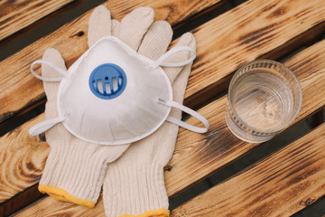 Mask, gloves are lying on the wooden table background. Glass of water is standing on the wooden background. Safety.