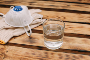 Mask, gloves are lying on the wooden table background. Glass of water is standing on the wooden background. Safety.