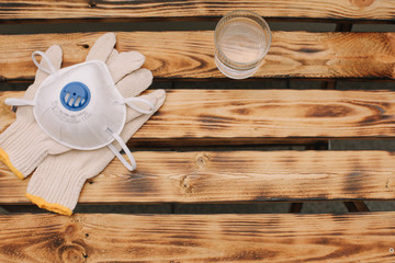 Mask, gloves are lying on the wooden table background. Glass of water is standing on the wooden background. Safety.