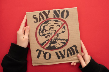 partial view of woman holding cardboard placard with say no war to war lettering and explosion in stop sign on red background