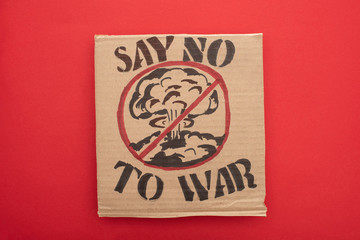 top view of cardboard placard with say no war to war lettering and explosion in stop sign on red background