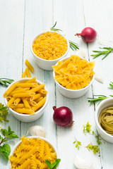 uncooked pasta variations and fresh spices on white wooden table