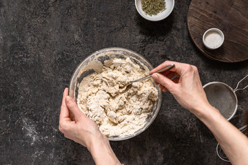 Girl kneads a dough for baking homemade bread on a black stone table with a fork. Cooking at home ourselves