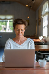 Obraz na płótnie Canvas Happy mature beautiful woman with short hair using laptop inside coffee shop
