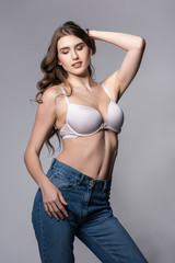 Fototapeta premium seductive girl in bra and denim jeans standing isolated on grey