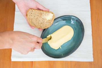Hands of woman with toast and knife cutting butter on table with napkin. Closeup shot, top view. Traditional bread or breakfast concept