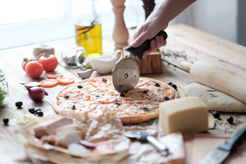 male hands are cooking pizza with sausage and ingredient on the wooden table in rustik style