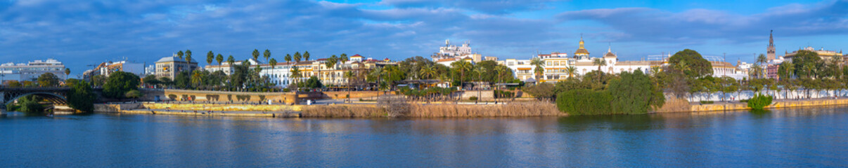 Fototapeta premium Panoramic view of the waterfront of the Guadalquivir River in Seville, Andalusia, Spain. On a warm winter evening, people relax and stroll along the waterfront.