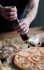 male hands are cooking pizza with sausage and ingredient on the wooden table in rustik style