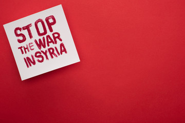 Top view of white placard with stop war in Syria lettering on red background