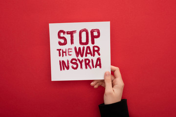 partial view of woman holding white placard with stop war in Syria lettering on red background