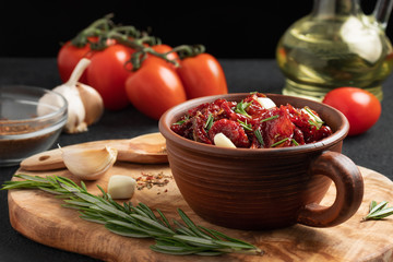 Sun-dried tomatoes with garlic, rosemary and spices in a clay bowl on an olive wood cutting board