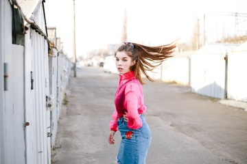 Model girl wagging her tail confidently on the street near the garages in a denim skirt and pink blouse. Street style trendy portrait