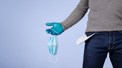 Male half body view. A hand protected with surgical gloves, holds some hygienic mask and shows the pocket of his empty pants. Concept of crisis and economic recession caused by coronavirus and covid19