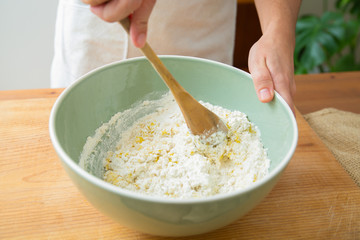 Cook mixing ingredient and wheat flour with wooden spoon in ceramic bowl. Dough preparation for homemade pastry and bread. Studio shot. Side view. Cooking and baking at home concept