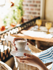 Morning at the cafe. A Cup of cappuccino with cinnamon. The girl collects foam with a spoon. The Cup is white. It's Sunny and warm outside. The atmosphere of an Italian restaurant or cafe. 
