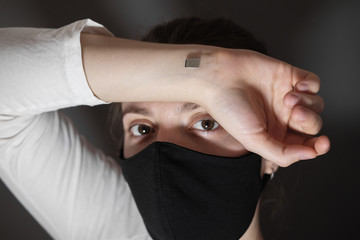 A microchip implanted on a person's hand during a coronavirus disease. A woman in a black protective medical mask.