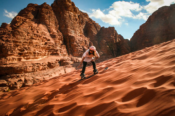 Wadi Rum, Jordan- Woman sandboarding on deep red sand dune. 