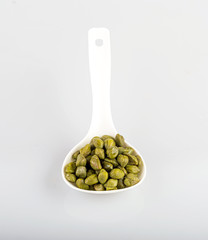 capers in a white spoon, isolated on a white background
