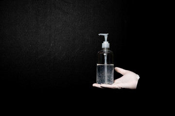 Human hands in the gloves holding a bottle of sanitizer on the plain black background. Disinfection and germ protection Prevention measures during the epidemic of Covid-19.