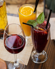 Two cold lemonades-orange and blackcurrant. A glass of red wine. With ice. The glasses are on the table. Alcoholic and non-alcoholic beverages. Summer terrace. Menu for bars and cafes. Vegetarian.