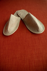 Comfortable luxury house or hotel slippers made from sackcloth on the bright red textile background. Shoes to wear indoors