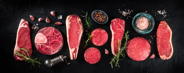 Various cuts of meat, shot from above on a dark background with condiments, a flat lay panorama