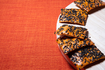 Fototapeta na wymiar Crispy brown baked biscuits with black sesame seeds on the top of wooden board placed on the left side of the frame, Bright red textile backdrop for copy space.Restaurant of cafe bites for tea, coffee