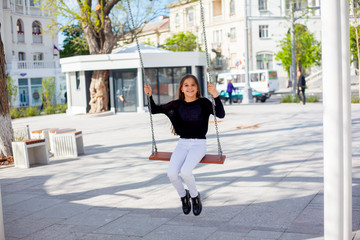 Style preteen girl dressed fashion black and white clothes riding a swing and walking outdoor in the street