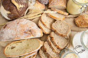 Top view of wheat and rye whole grain loafs and baguettes cut in slices, corn flour in jar and ears. Bakery or traditional bread concept