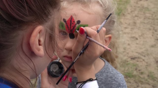 Children face painting. Artist painting little girl like ladybird. Gimbal motion