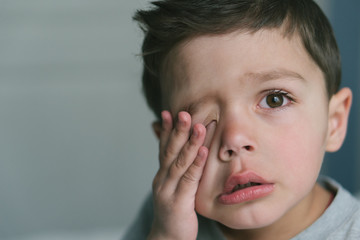 frustrated toddler boy touching face at home