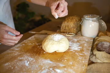 Hand dusting flour on kneaded dough for homemade pastry laying on wooden board. Fresh cereal loaf flour in glass jar. Studio shot. Side view. Cooking and baking at home concept