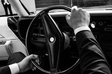Retro car. Black. On Polished bumpers. The man keeps his hands on the steering wheel. Black and white photo.