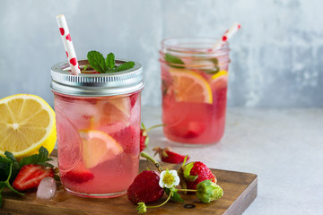 Summer drink refreshing. Lemonade with fresh strawberries, ice and lemons on a light stone countertop. Copy space.