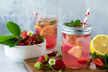 Summer drink refreshing. Lemonade with fresh strawberries, ice and lemons on a light stone countertop.