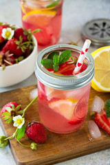 Summer drink refreshing. Lemonade with fresh strawberries, ice and lemons on a light stone countertop.
