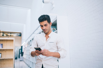 Cheerful young male student using smartphone in library