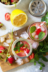 Fototapeta na wymiar Summer drink refreshing. Lemonade with fresh strawberries, ice and lemons on a light stone countertop. Top view flat lay background.