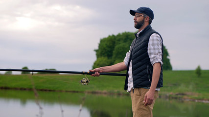 A young bearded man fishing on a lake, a fisherman holding a fishing rod in his hands