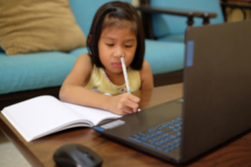 Thai girl in online learning class at home during the COVID-19 situation. Student writing the book and learning form notebook during quarantine. Blurred focus. Online education, home school concept.
