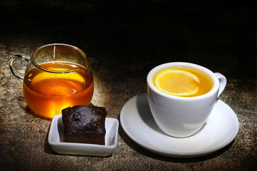 A cup of tea with lemon served with honey and a slice of chocolate cake. 
