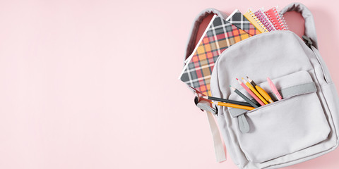 Back to school concept. Backpack with school supplies, pens, pencils, notebook on pastel pink background. Flat lay, top view, copy space, banner