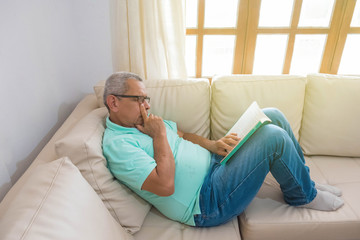 Obraz premium Retired man reading a book on the sofa in his home